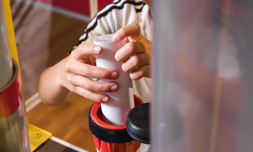 Close-up of a student's hands putting a letter into the pneumatic tube.