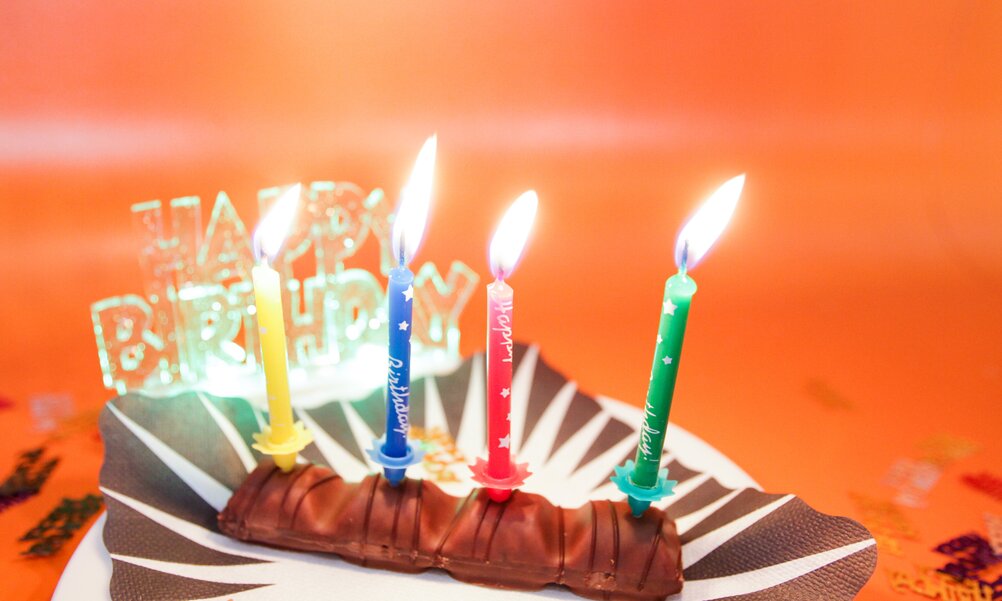 Auf einem Tellerchen liegt ein Schokoriegel mit vier brennenden Kerzchen und einem Happy-Birthday-Schriftzug.