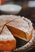 A pumpkin pie with icing sugar on top is lying on a glass plate. A piece of the cake is missing.