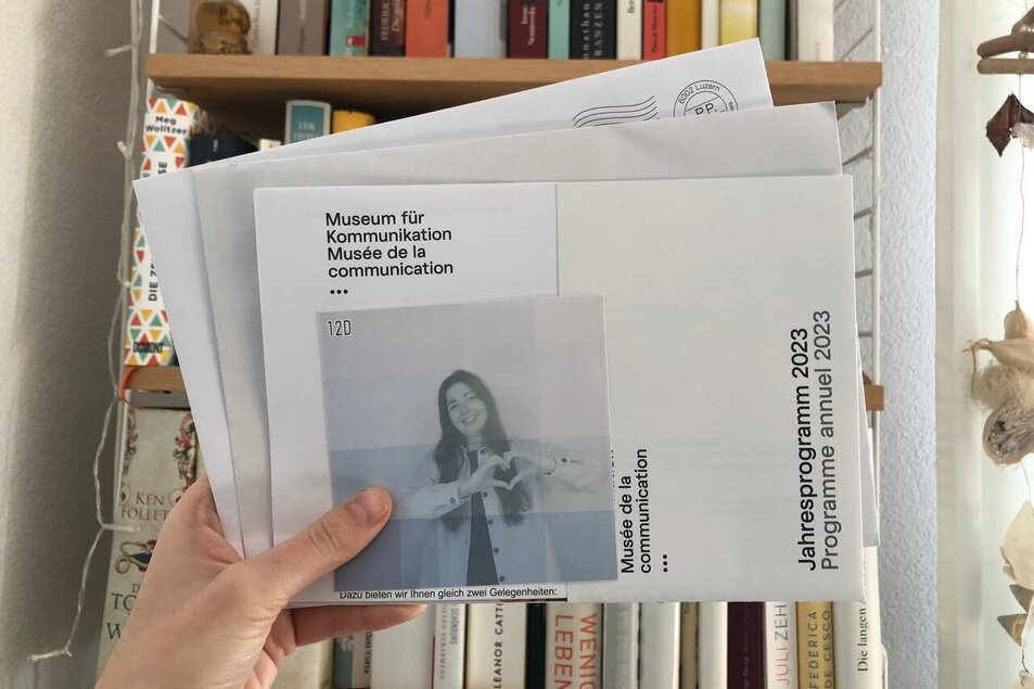 Post Eine Hand hält einige Briefe ins Bild, darauf das Bild einer jungen Frau. Im Hintergrund ein Bücherregal. - vergrösserte Ansicht