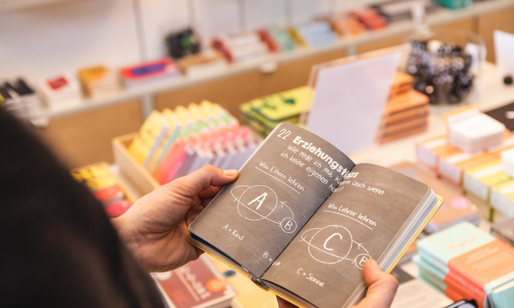 A person is looking at a book with communication theories. The display of a shop can be seen in the background.