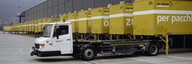 Blick auf ein grosses Graues Gebäude. Davor viele Postlastwagen.  - vergrösserte Ansicht