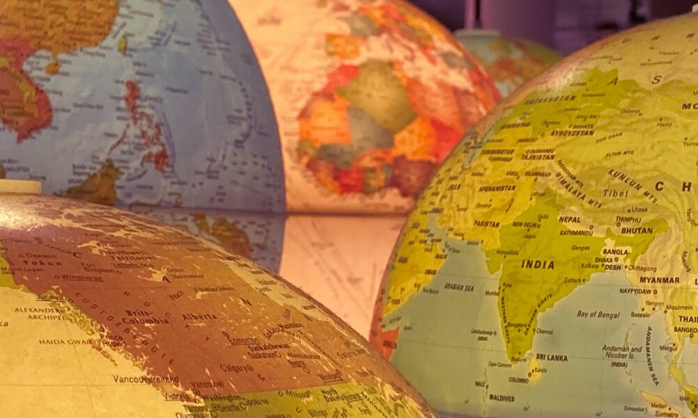 Verschiedene Weltkugeln sind hintereinander zu sehen, darauf verschiedene Erdteile.