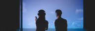 Two people sit in front of a projection of a sky with clouds. - enlarged view