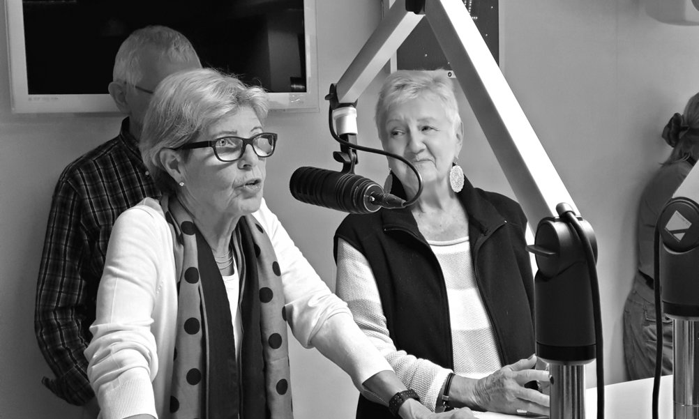 Zwei Seniorinnen von Radio Silbergrau stehen am Radiomikrophon und moderieren.