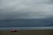 Etwas Strand mit einem kleinen roten Rettungsbot und einer Möwe. Dahinter das Meer und grauer Himmel.