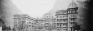 Historische schwarz-weiss Aufnahme: Eine Wiese mit einzelnen Büschen, dahinter das grosse zweiflüglige Hotel Bear. Hinter dem Hotel ist das leicht verschneite Hochgebirge zu sehen. - vergrösserte Ansicht