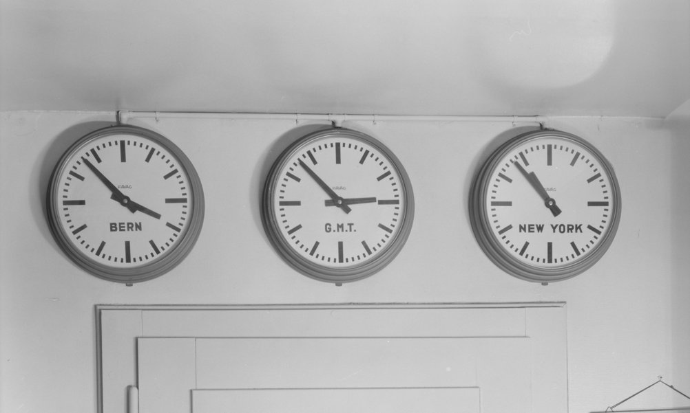 Drei Uhren an einer Wand zeigen unterschiedliche Zeitzonen an: Bern, Greenwich Mean Time und New York.