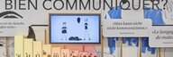 Blick auf eine Wand in der Ausstellung des Museums für Kommunikation: Texte, Bildschirme und Illustrationen. - vergrösserte Ansicht