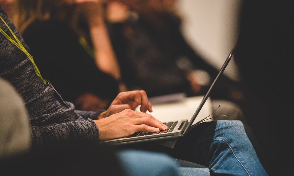 A person with a laptop on his knees is taking notes.