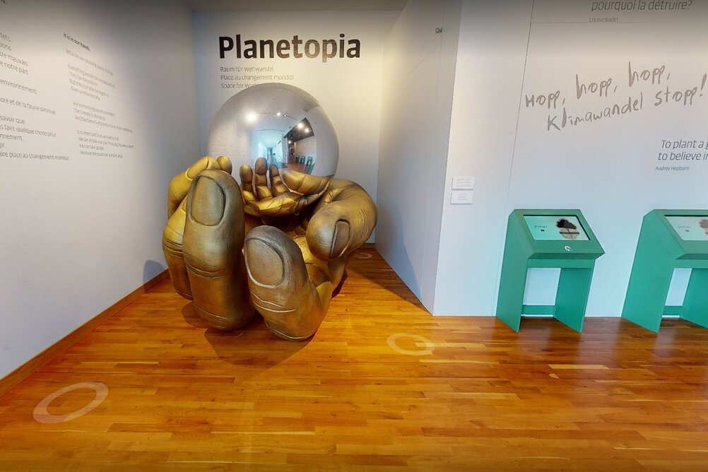 Bild des Eingangs zur Ausstellung Planetopia mit einer riesigen goldenen Hand, die einen silbernen Spiegelball hält.