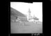 Schwarz-Weiss-Fotografie. Auf einer Wiese in den Bergen stehen vereinzelte Kühe und grasen. Dahinter eine mittelalterliche Kirche mit Turm und Bauernhäuser.