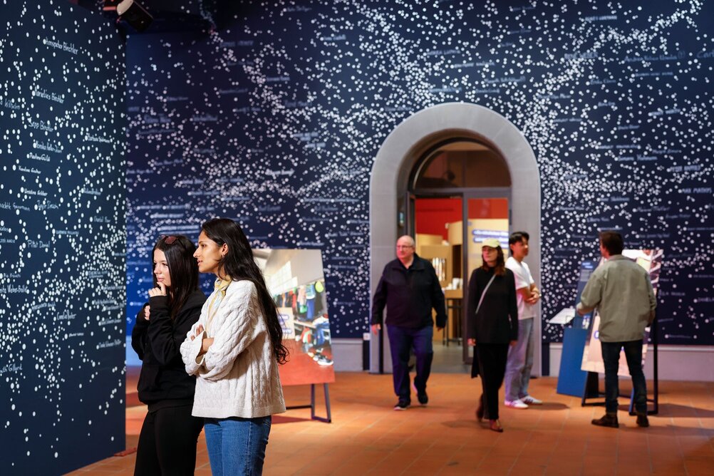 Vom Glück vergessen Menschen stehen vor einer Wand mit Punkten und Namen.