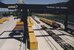 Blick auf einen schwarzen Containerkran von der Post. Es stehen verschiedene Container an der einen Seite während auf der anderen Gleise sind, auf denen eine leerer Güterzug bereit steht.  - vergrösserte Ansicht