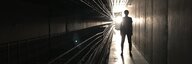 Ein dunkler Gang, am Ende eine Lichtquelle - im Gegenlicht steht eine Person. - vergrösserte Ansicht