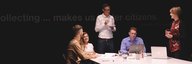 Five people sit at the end of a large table and discuss something. In front of them are work utensils such as laptop, pens, notepaper. - enlarged view