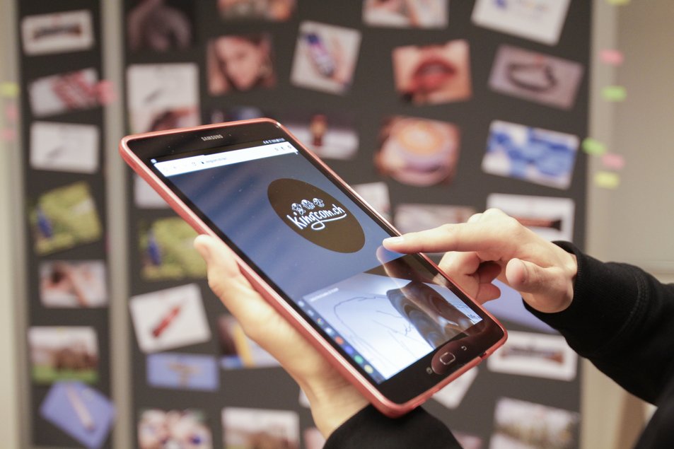 KingCom Ein Tablet vor einer Wand mit vielen Post-It-Notizen. Eine Hand bedient auf dem Tablet die King-Com-Webseite.