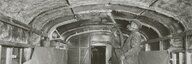 Auf dem schwarz-weiss Foto ist das rohe, unverkleidete Innere eines Eisenbahnwagens zu sehen. Eine Person mit Atemmaske führt einen Schlauch durch den Wagen und spritzt Asbest an die Decke. - vergrösserte Ansicht