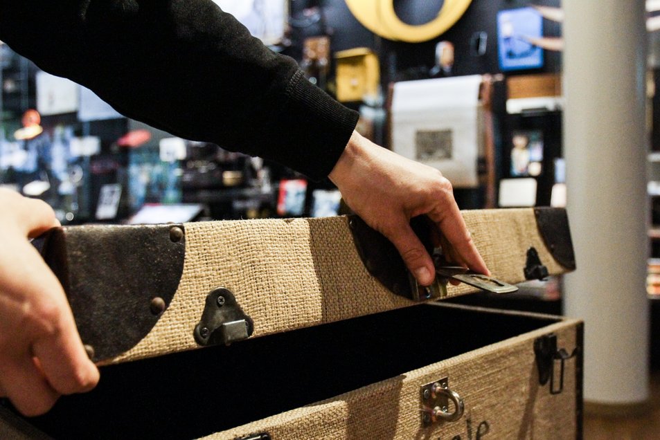 Postkiste Eine Hand öffnet in der Ausstellung eine grosse Post-Kiste. Im Hintergrund sind Ausstellungsobjekte zu sehen.