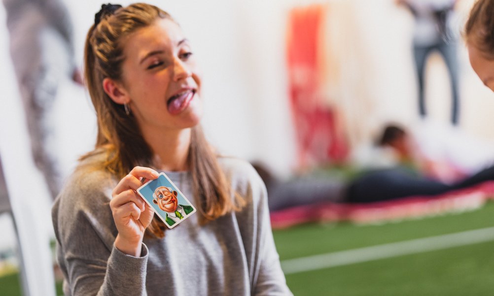 A young woman shows a card with a grimace on it and then recreates this grimace herself.