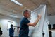 Eine Person steht in einem Sitzungszimmer vor einem Flipchart und notiert etwas, andere sind im Hintergrund am Diskutieren.