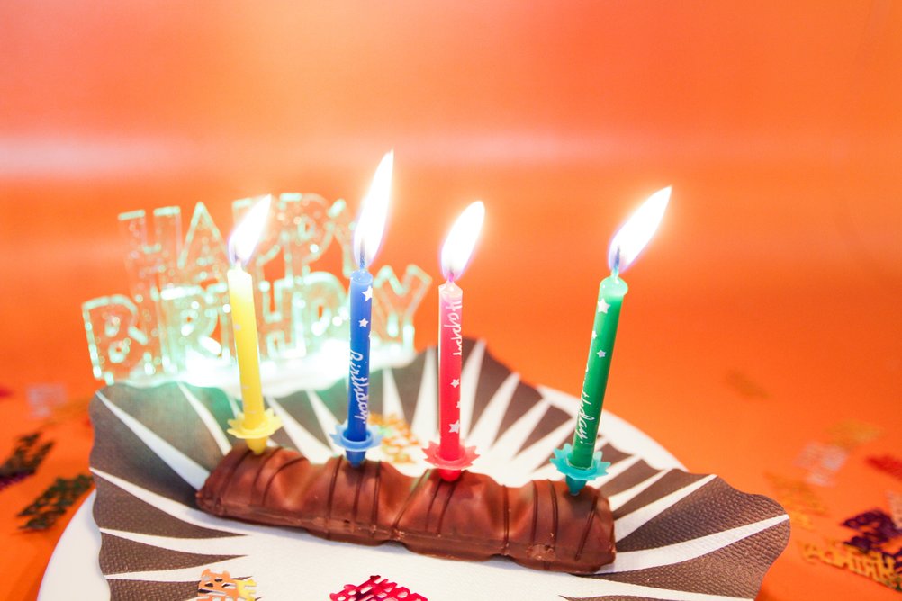 Sur une petite assiette se trouve une barre de chocolat avec quatre bougies allumées et un panneau "Joyeux anniversaire".