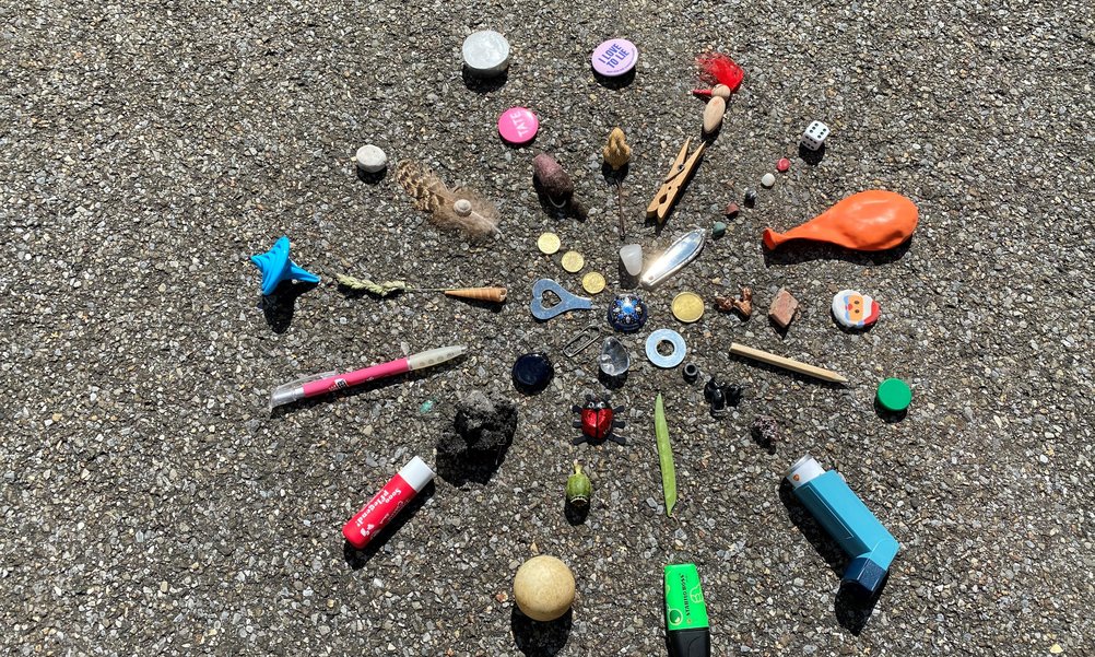 Sur le sol se trouve un fatras de petits objets disposés en forme de rayon : Des boutons, des stylos, un ballon et bien plus encore.