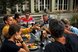Menschen sitzen draussen um einen Tisch und essen miteinander. Sie reichen sich Essen weiter. Es ist Sommer.