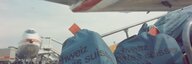 Blick auf Schweizer Postsäcke, die auf einem Förderband stehen welches in Richtung Frachtraum einer Boeing 747 der Swissair führt. Im Hintergrund ist ein zweites Flugzeug zu sehen.  - vergrösserte Ansicht