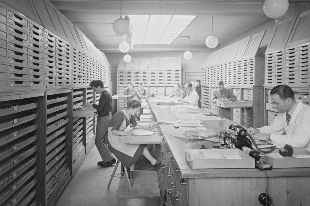 Mehrere Personen in einem Archivraum sortieren Dokumente.