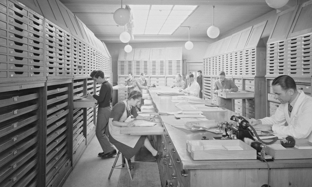 Several people in an archive room sort documents.