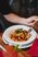 A person sits in front of a plate of pasta with sauce.