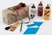 Im Bild zu sehen ist eine Tragtasche voller Farbflecken. Daneben stehen Farbflaschen (weiss, rot, gelb), Pinsel, ein Bleistift und Formvorlagen (Pfeil, Rhombus). - vergrösserte Ansicht