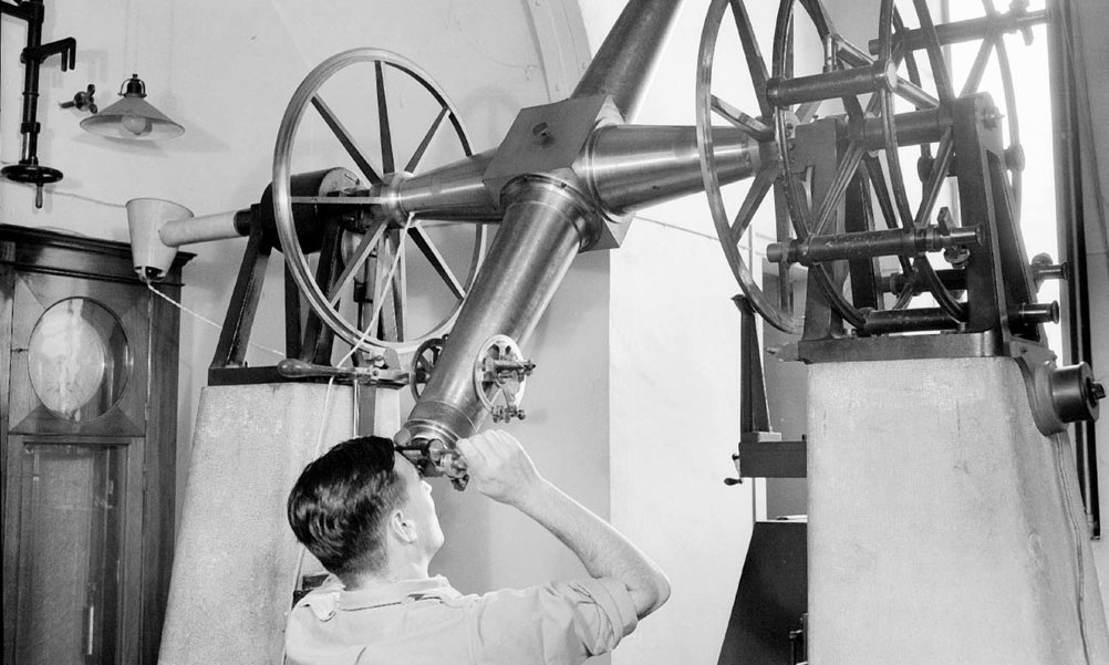 A black and white image of a man looking through an old-fashioned telescope.