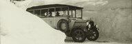  Sur cette photographie en noir et blanc, on peut voir un bus postal Saurer sur une route enneigée. De chaque côté de la route, on peut voir de hauts murs de neige. - vue agrandie