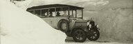 Auf dieser Schwarz-Weiß-Fotografie ist ein Saurer-Postbus auf einer verschneiten Straße zu sehen. Auf beiden Seiten der Straße sind hohe Schneewände zu sehen. - vergrösserte Ansicht