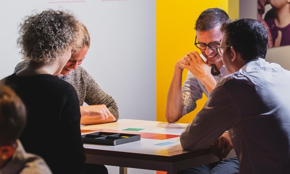 Four contented people sit at a table and play a game.