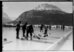 Schwarz-Weiss-Fotografie. Auf einem zugefrorenen See spielen Menschen Curling. Im Hintergrund ein grosser Berg.