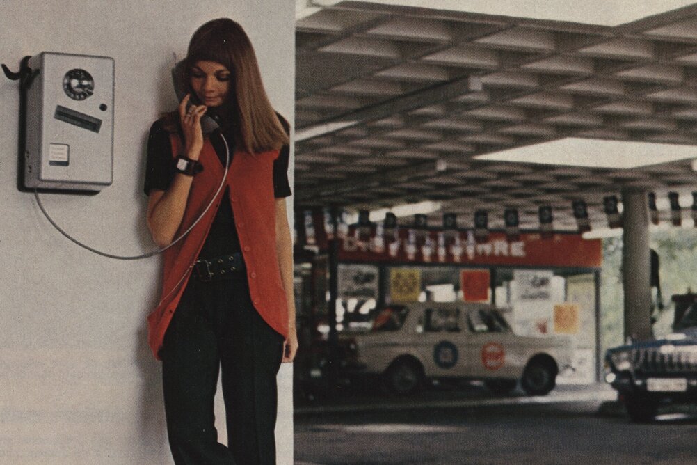 Ein Bild aus den 1970er-Jahren. Lässig lehnt eine junge Frau an die Wand neben einem Münztelefon, den Hörer in der Hand.