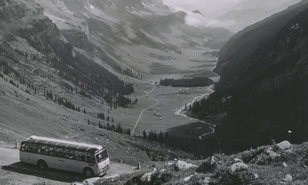 Historical picture of a post bus on a pass road, the valley floor can be seen in the background.