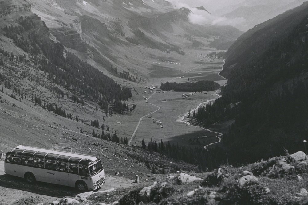 Historisches Bild eines Postautos auf einer Passstrasse, im Hintergrund ist der Talboden zu sehen.
