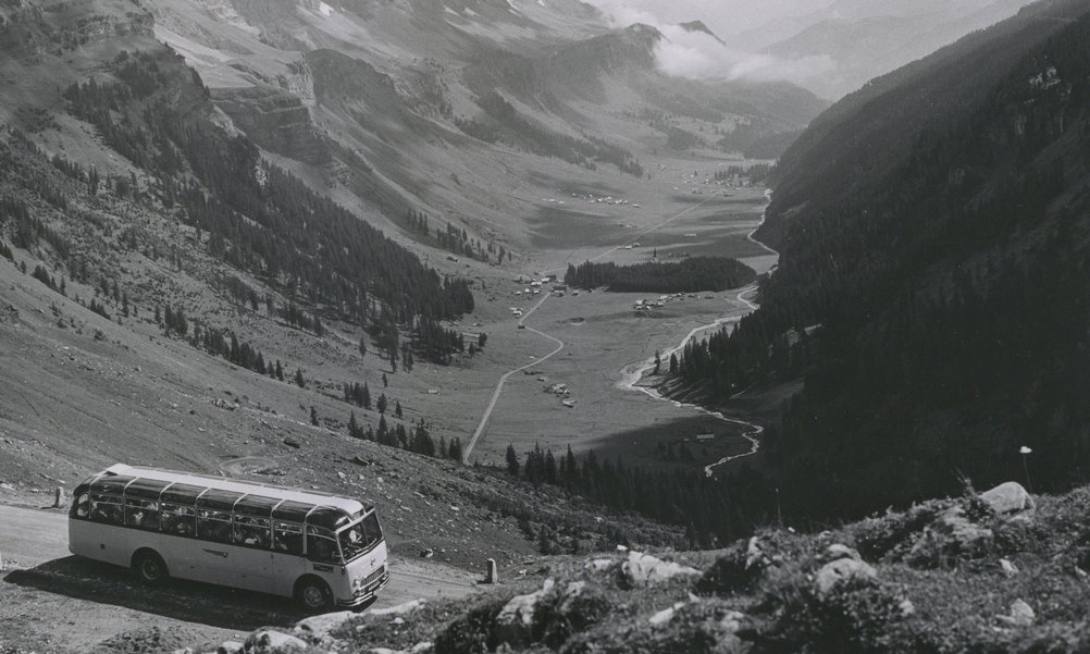 Historisches Bild eines Postautos auf einer Passstrasse, im Hintergrund ist der Talboden zu sehen.