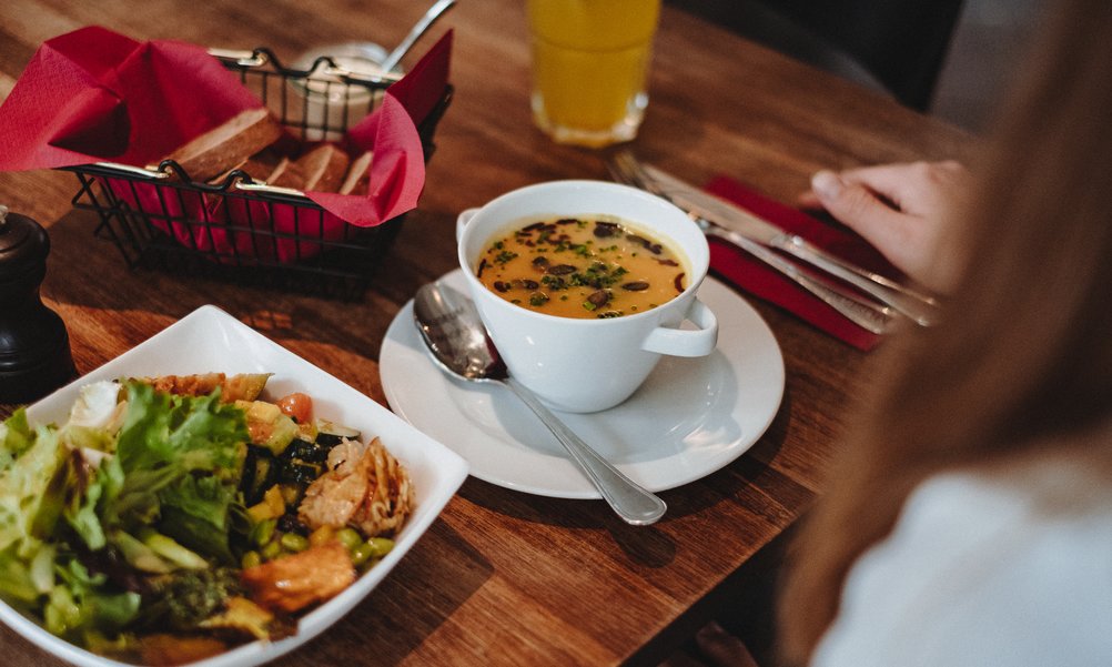 Over one person's shoulder we look at the lunch table with salad plate and soup.