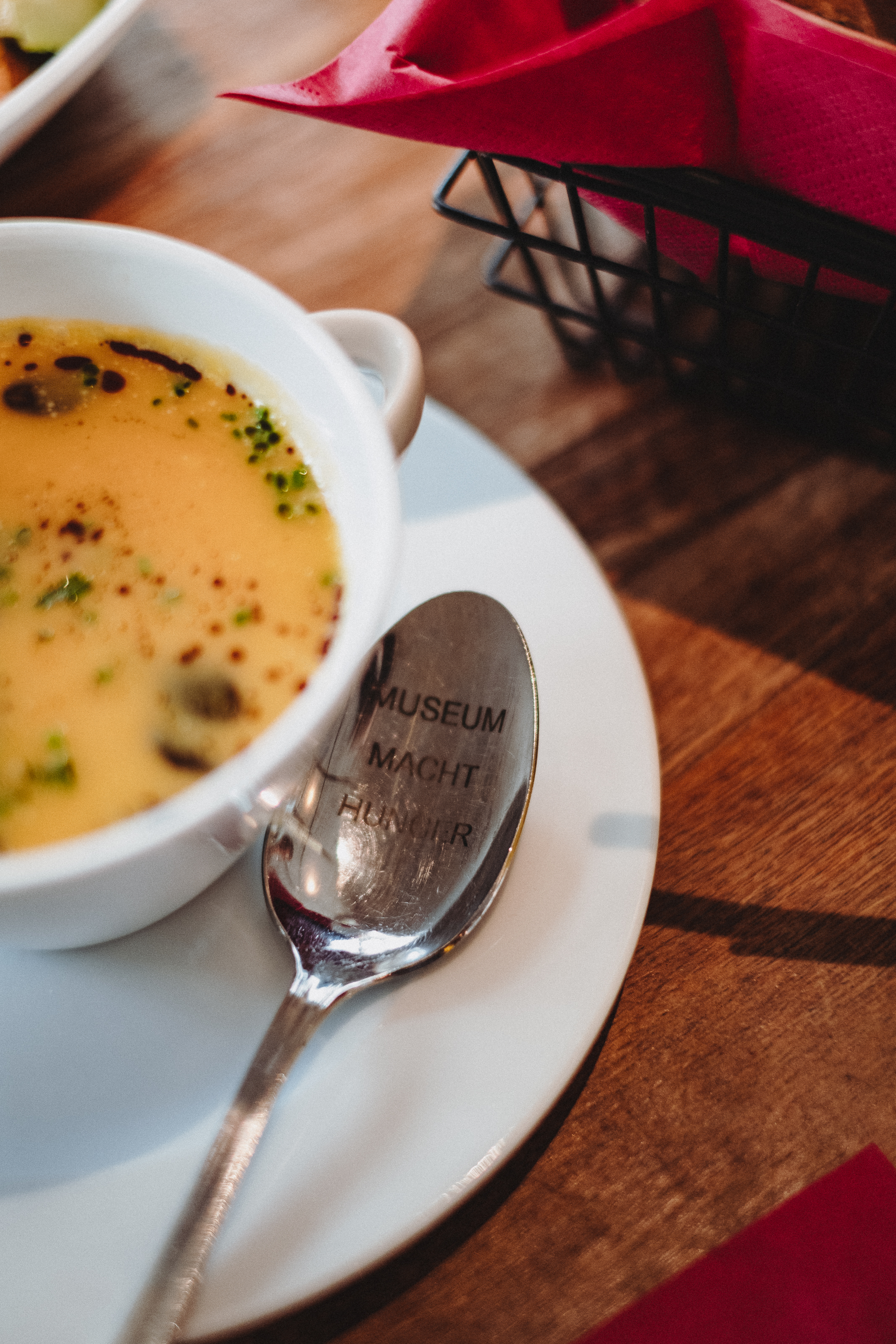 There is a plate of soup on a table. Next to it is a spoon with the words "Museum makes you hungry". - enlarged view